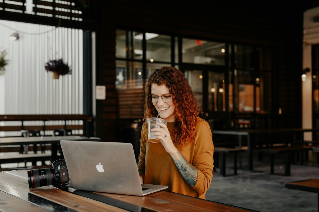 Personne souriante travaillant sur un ordinateur portable à une table en bois, ambiance lumineuse et professionnelle