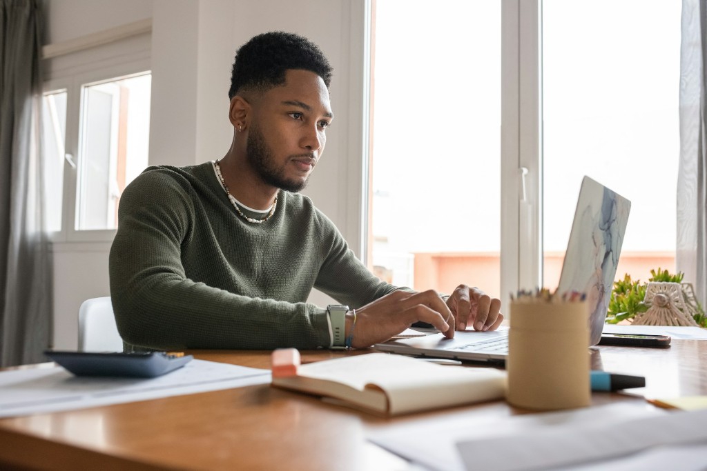 Professional working at a laptop on a wooden desk in a bright office with natural light from a window
