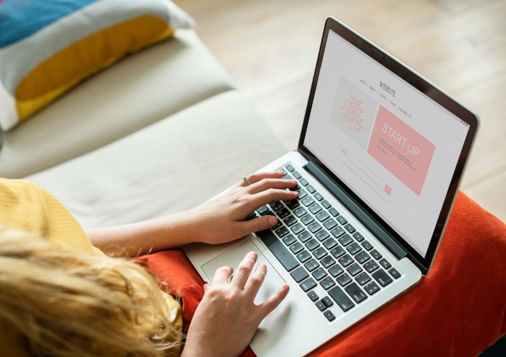 Vue de dessus d’une femme travaillant sur un ordinateur portable, un site Web affiché à l’écran, assise sur un sofa.