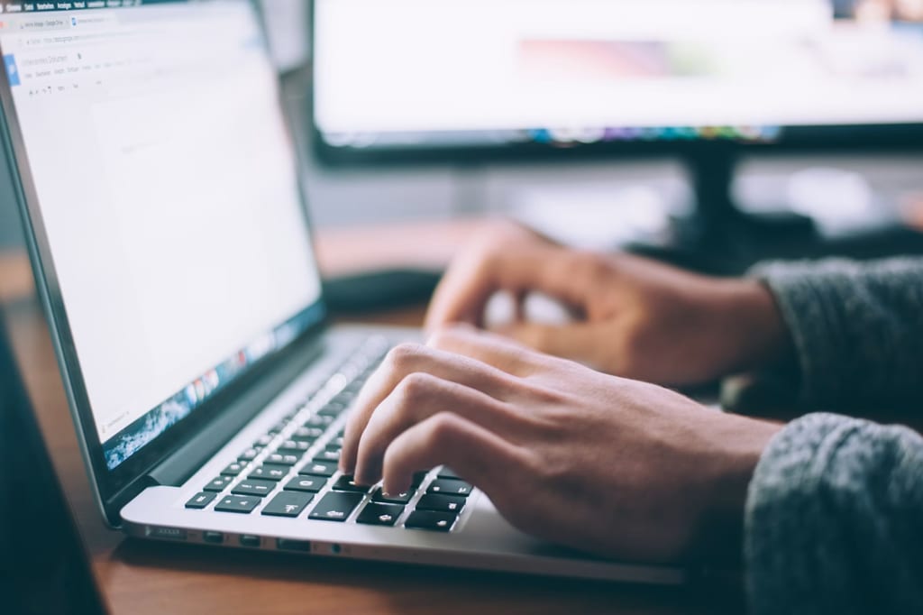 Des mains qui tapent sur un ordinateur portable rédigeant un texte en langage clair dans un document vierge.